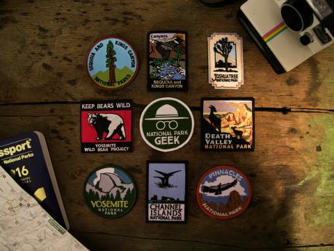 National park patches spread out on a table with a map, passport, and camera.